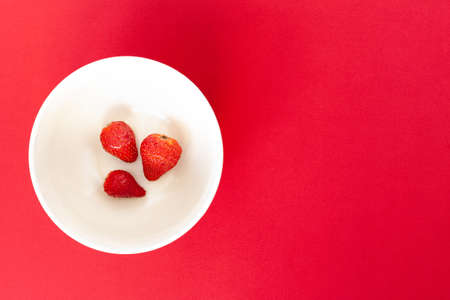 three red strawberries on a white plate on the red background, isolated.