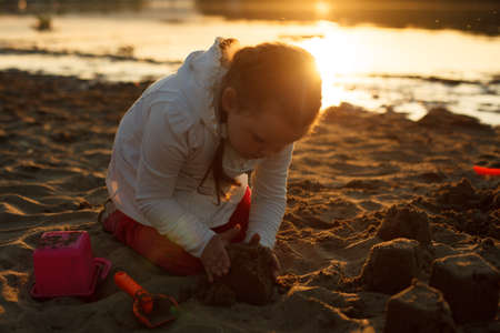 a girl plays with sand on a sandy beach on the river Bank during sunset.