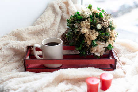 A Cup of coffee or tea, dry flowers and white, red candles, a red wooden box on a beige blanket.の写真素材