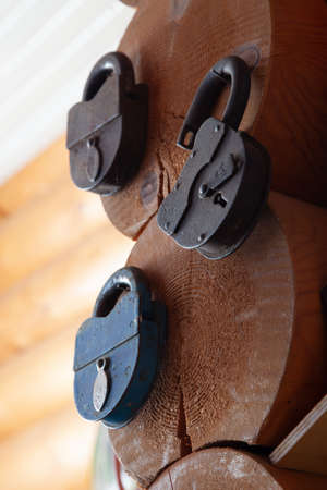three large old metal locks hang on the wall of a wooden log houseの写真素材