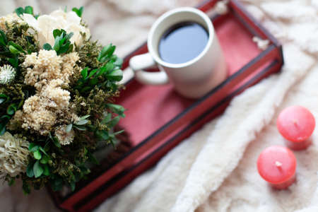 A Cup of coffee or tea, dry flowers and white, red candles, a red wooden box on a beige blanket.の写真素材