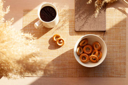 A cup of coffee, dry flowers, barankis, notepad on wooden table. Brown and white.の写真素材