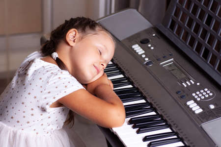 child girl in white dress sleeps on the keys of an electronic piano, synthesizerの写真素材