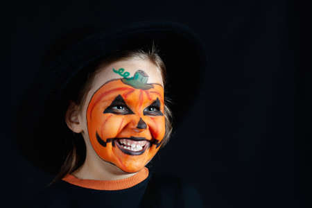 girl in a black hat and pumpkin makeup for Halloween look sideways on a black background, mock upの写真素材