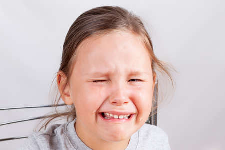 girls face close-up in tears, the child is upset and crying on a gray background, isolated