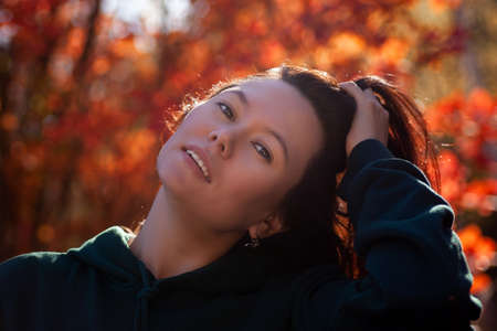 portrait of a beautiful Asian youth woman with a hand in her hair in a red autumn forest at sunset