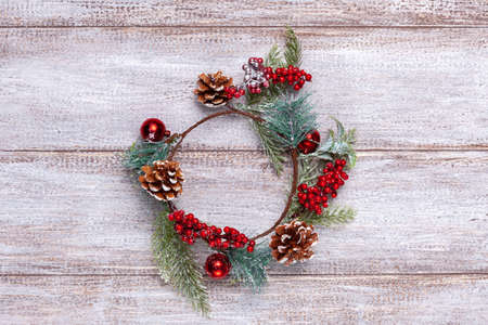 Christmas wreath of fir branches, cones and red berries on a wooden backgroundの写真素材