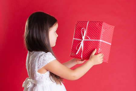 close up of girl in white dress with a side, handing someone a gift box for Christmas or birthday on a vivid backgroundの写真素材
