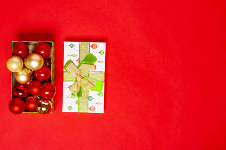 open from green gift box with red and gold balls for the Christmas tree, next to the lid with a bow on a red backgroundの写真素材