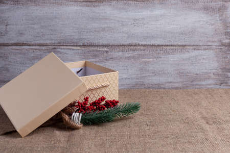postcard from beige gift box with open lid and sprig of Christmas tree with decorations on wooden...