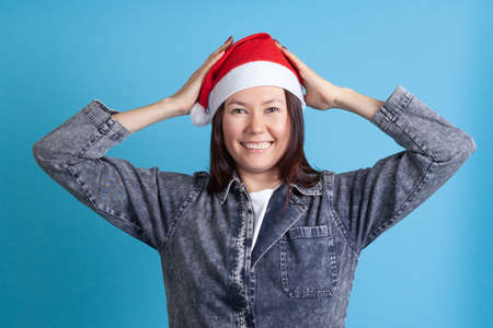 smiling Asian young woman in a Santa hat holds her head with her hands, isolated on a blue backgroundの写真素材