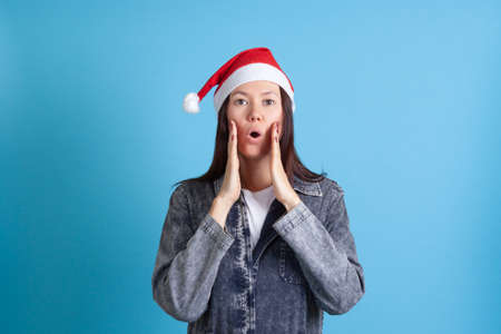 surprised Asian young woman rounds her mouth and does exercises for youthful facial muscles, isolated on blue backgroundの写真素材