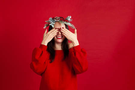 close-up portrait of a happily laughing Asian young woman in a wreath covering her eyes with her hands waiting for a gift and a new years miracle,の写真素材