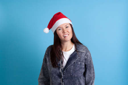 mock up of a serious, sexy Asian young woman in a Santa hat biting her lip with her teeth on a blue backgroundの写真素材