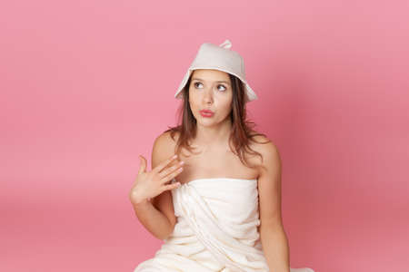 the girl in the towel on the body and a felt hat for sauna fans face from the heat, isolated on pink...