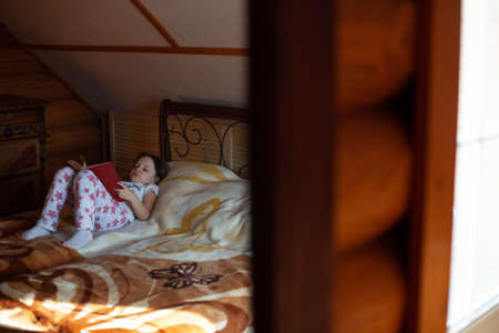reflection in the mirror a girl reading a book is lying on her back on a wrought iron bed in the log cabin bedroomの写真素材