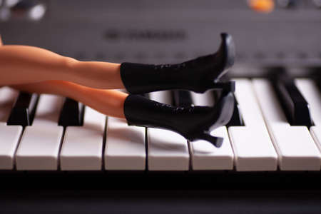 Close-up slim plastic legs in black toy rubber boots with high heels lie on piano keysの写真素材