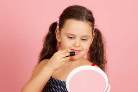 close-up portrait of a smiling happy girl with painted lashes and a peach-colored shiny lipstick, isolated on a pink backgroundの写真素材
