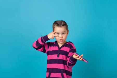 dynamic portrait of girl with pigtails looking at camera, holding phone in her hand and showing victory sign near eye, isolated on a blue backgroundの写真素材