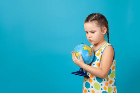 close-up portrait of five-year-old girl in white summer dress hugging globe and thinking about the future of the Earth, isolated on a blue backgroundの写真素材