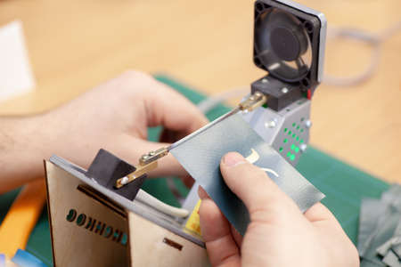 hands of a man sealing, cutting off the edges of labels and tags for clothing on an electric string...