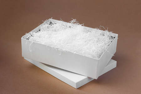 white shredded paper in a white open box on the lid on a paper beige background for protection...