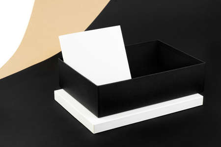 mock-up in the minimalist style of an open black box on a white lid and a white notepad or sheet on a background of beige, black, white paperの写真素材