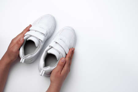 mock up two hands of a woman holding a childs white sneakers with fasteners with a blank space for...
