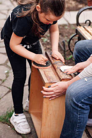 mom and daughter together sandpaper an old wooden box from polish, preparing an antique cabinet for repair, an eco-friendly business of reusing thingsの写真素材