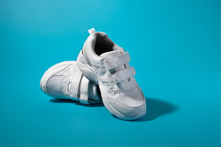 the back of one white childrens running shoe stands on top of another lying on its side on an isolated blue paper backgroundの写真素材