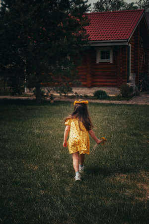 rear view of the back of a running preschool girl in a yellow dress in the backyard on a summer day