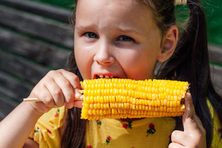 Close-up portrait of a girl with corn. Girl eating sweet boiled corn for lunch outdoorsの写真素材