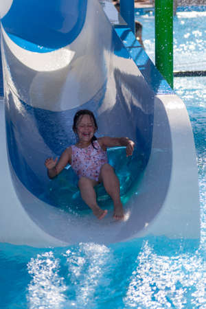a screaming girl in a pink swimsuit ride on an inflatable circle from a water slide in a water park