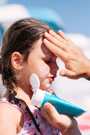 a parent puts sunscreen on a girls face from a blue tube by the pool at a family hotel