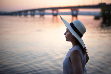 profile portrait of a woman in a hat on a mini trip along the river at sunsetの写真素材