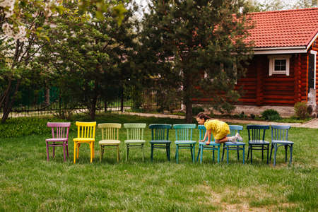 childrens birthday party outdoors, the birthday girl crawls along a line of colorful chairs waiting for guests and childrenの写真素材
