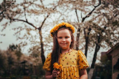 portrait at sunset of a cute, charming girl in a dress and a wreath of dandelions on her head, a girl with a bouquet of dandelions outdoor at sunsetの写真素材