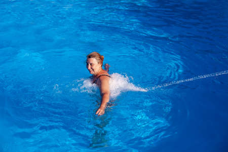 A beautiful, Caucasian woman enjoys a back and neck hydro massage with a jet of water in an outdoor...