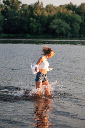 Photo of a running blonde in profile. A young woman in a white top and shirt and denim shorts runs...
