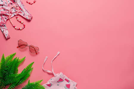 Flat lay with summer accessories. Childrens summer accessories, sunglasses, swimsuit, shorts, tropic leaves with copy space on the pink isolated background flat layの写真素材