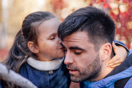 close up man and girl family portrait. awesome dark-haired man and whispered little girl in blue jacket at autumn park backgroundの写真素材