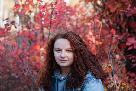 woman portrait close up. woman with long curvy brown hair in autumn forest with red bush on...