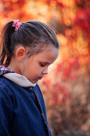 side view girl portrait. beautiful little girl in blue jeans jacket look down at autumn forest backgroundの写真素材