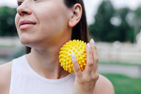 close-up of neck of young woman doing self-massage with spiky rubber ball to relax and relieve tension in muscles outdoorsの写真素材