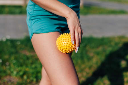 side view of thin athletic body of a young woman doing hip massage with spiky ball in park in summerの写真素材