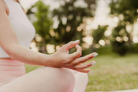 blurred close - up of woman legs sitting in lotus position and meditating and fingers in Gyan mudra on summer dayの写真素材
