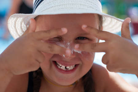 Portrait of happy child. Smiling little girl in white  hat makes faces and enjoys her summer...