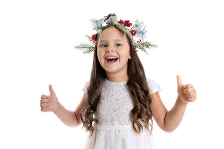 portrait of joyful, contented Caucasian girl in Christmas wreath, white dress and giving thumbs up, isolated on white background, the concept of successful New Year giftの写真素材