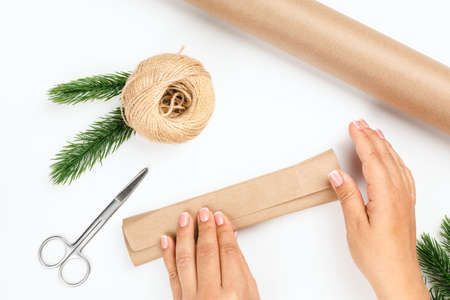 woman hands pack box with New Year gift in brown paper on white isolated background