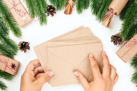 flat lay of two female hands holding stack of craft paper envelopes for greeting cards, Christmas...
